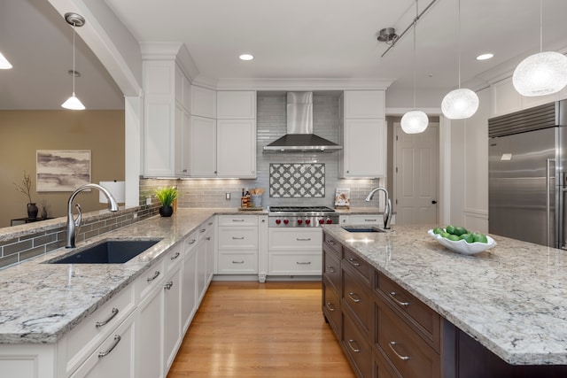 kitchen featuring pendant lighting, sink, appliances with stainless steel finishes, and wall chimney range hood