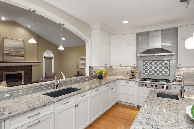 kitchen with white cabinetry, wall chimney range hood, sink, and hanging light fixtures