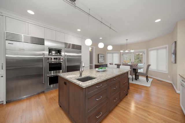 kitchen featuring white cabinetry, sink, light stone counters, built in appliances, and decorative light fixtures