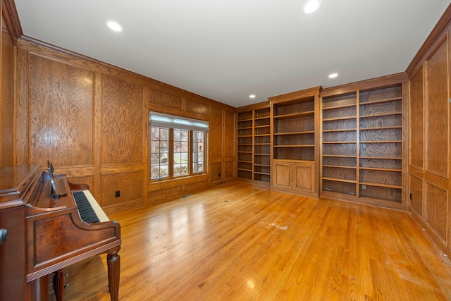 unfurnished living room with built in shelves, light hardwood / wood-style floors, and wood walls