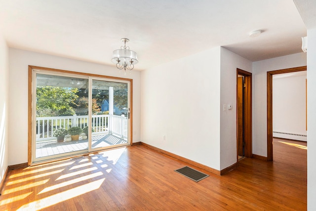 spare room with hardwood / wood-style floors, an inviting chandelier, and a baseboard radiator