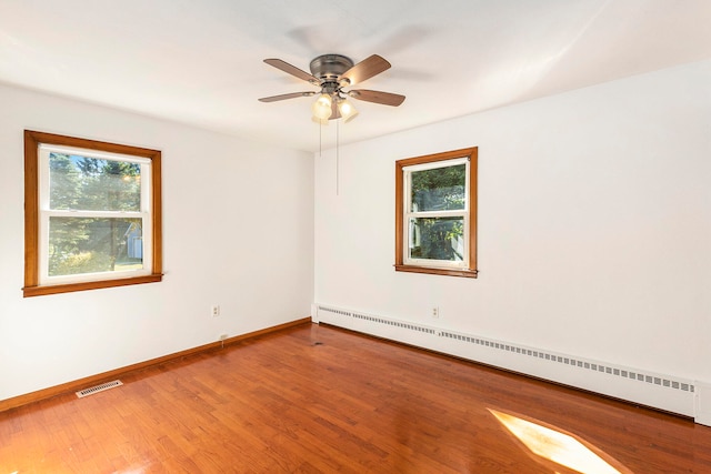 unfurnished room with ceiling fan, plenty of natural light, wood-type flooring, and a baseboard heating unit