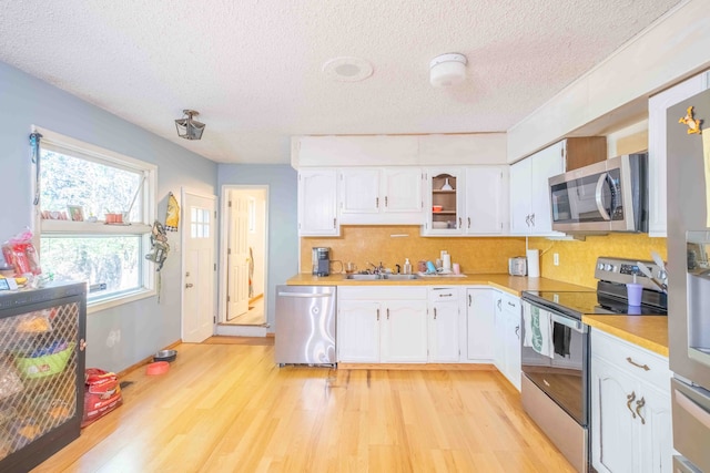 kitchen featuring white cabinetry, sink, light hardwood / wood-style flooring, a textured ceiling, and appliances with stainless steel finishes