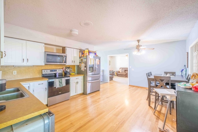 kitchen featuring white cabinets, sink, light hardwood / wood-style flooring, a textured ceiling, and appliances with stainless steel finishes