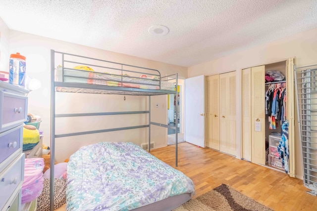 bedroom with wood-type flooring, a textured ceiling, and multiple closets