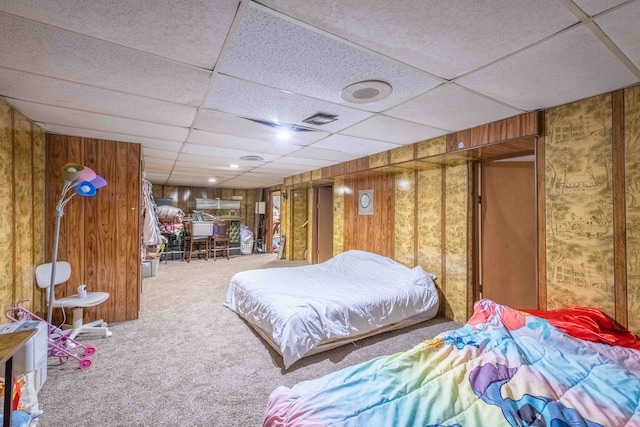 carpeted bedroom with a paneled ceiling and wood walls