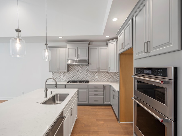 kitchen with gray cabinetry, sink, light hardwood / wood-style flooring, pendant lighting, and appliances with stainless steel finishes