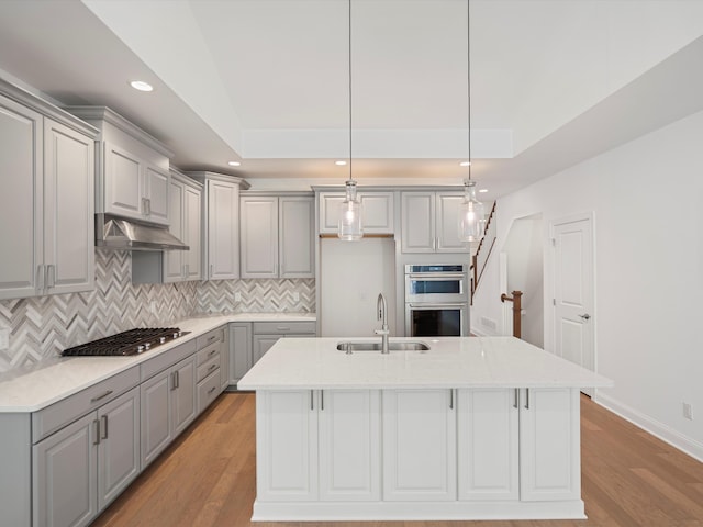 kitchen featuring a kitchen island with sink, sink, decorative light fixtures, and appliances with stainless steel finishes