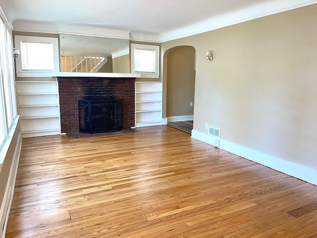 unfurnished living room featuring a brick fireplace, built in features, ornamental molding, and light wood-type flooring