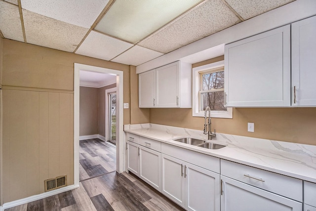 kitchen with a drop ceiling, white cabinetry, light wood-type flooring, and sink