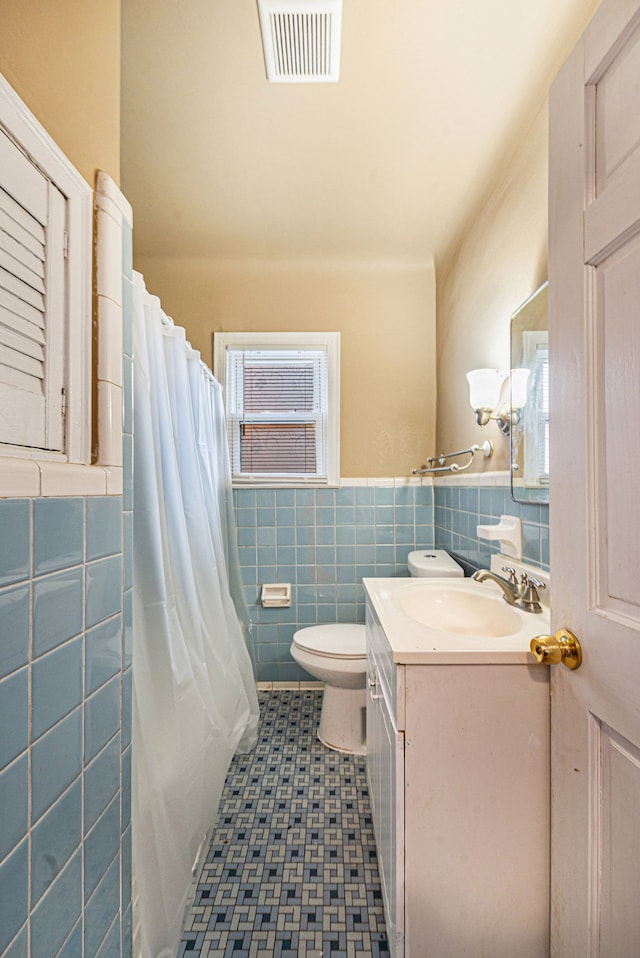 bathroom featuring vanity, toilet, tile walls, and walk in shower