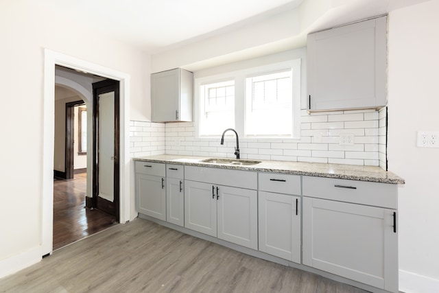 kitchen featuring gray cabinetry, sink, tasteful backsplash, light stone counters, and light hardwood / wood-style flooring