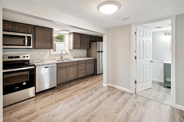 kitchen featuring sink, light stone counters, light hardwood / wood-style floors, dark brown cabinets, and appliances with stainless steel finishes