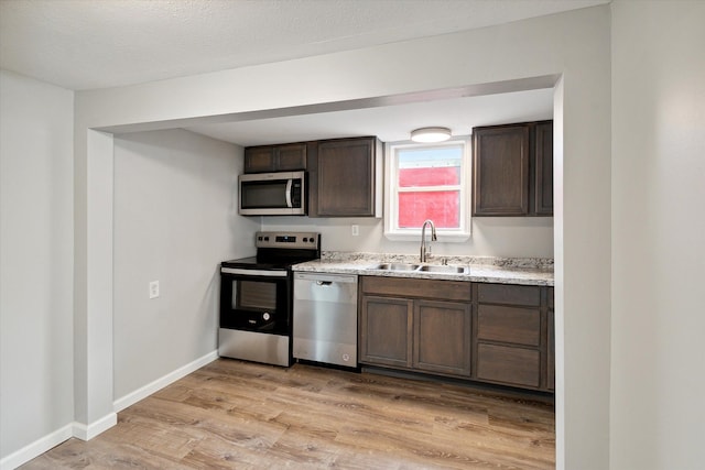 kitchen with appliances with stainless steel finishes, light wood-type flooring, dark brown cabinets, a textured ceiling, and sink