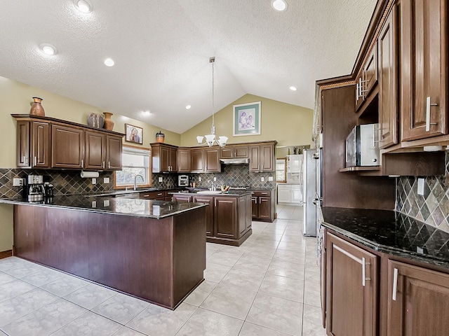 kitchen with decorative backsplash, dark stone counters, decorative light fixtures, a notable chandelier, and lofted ceiling