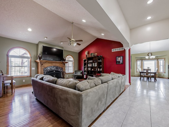 living room with a fireplace, a textured ceiling, light wood-type flooring, and ceiling fan with notable chandelier