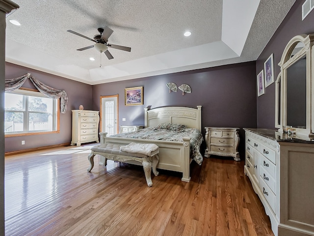 bedroom with a raised ceiling, ceiling fan, light hardwood / wood-style flooring, and a textured ceiling