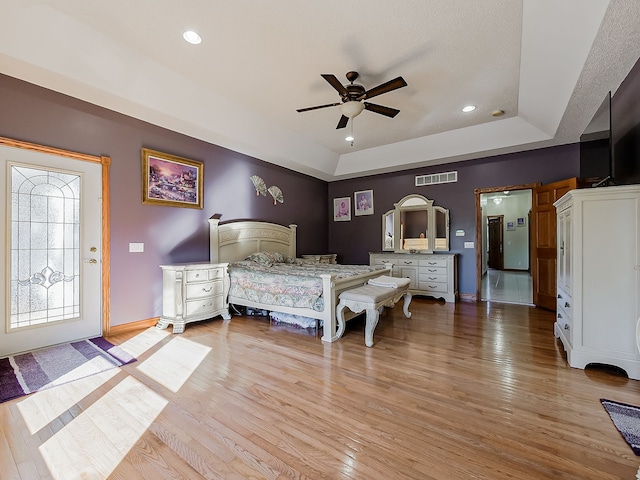 bedroom with a tray ceiling, light hardwood / wood-style flooring, and ceiling fan