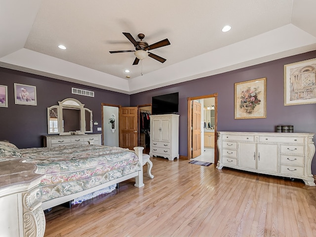 bedroom featuring ceiling fan, a raised ceiling, ensuite bathroom, light hardwood / wood-style floors, and a closet