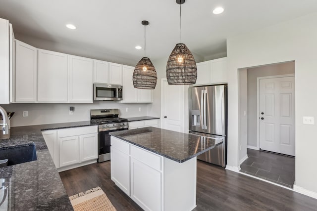 kitchen featuring stainless steel appliances, white cabinetry, hanging light fixtures, and dark stone counters