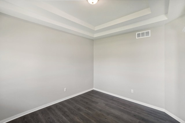 empty room with a tray ceiling, visible vents, baseboards, and dark wood-style flooring