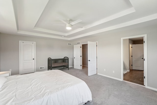 carpeted bedroom with a raised ceiling, baseboards, visible vents, and ceiling fan