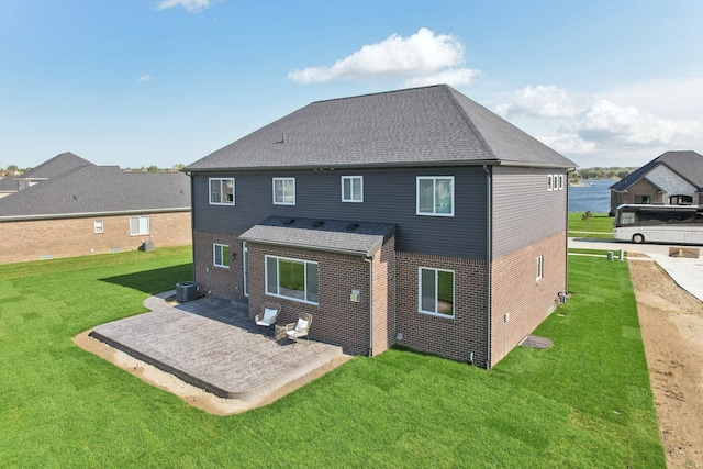 back of house with a lawn, a patio, central AC, roof with shingles, and brick siding