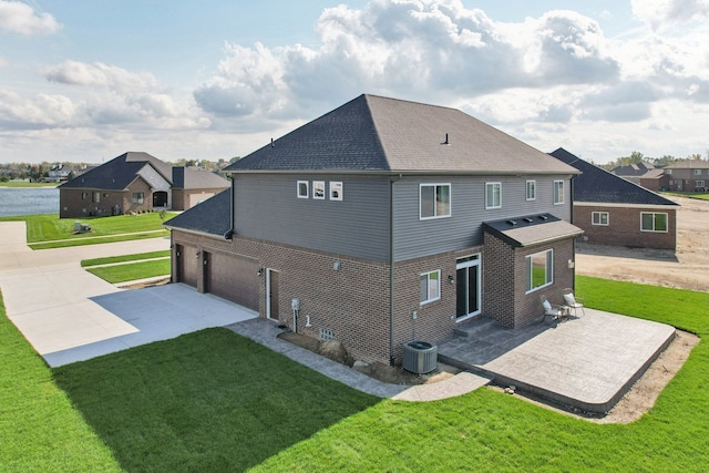 rear view of house with cooling unit, a garage, a lawn, and a patio area