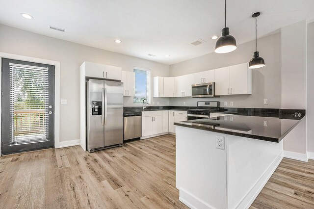 kitchen with white cabinets, decorative light fixtures, light wood-type flooring, and stainless steel appliances