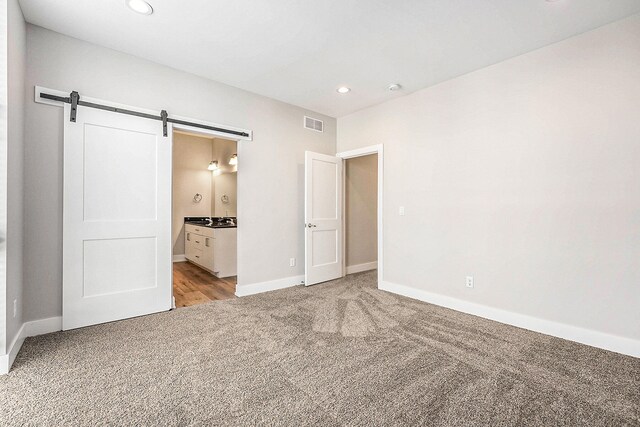 unfurnished bedroom featuring a barn door, light carpet, and ensuite bath