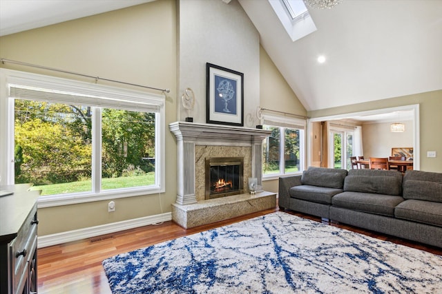 living room with high vaulted ceiling, light hardwood / wood-style flooring, a skylight, and a premium fireplace