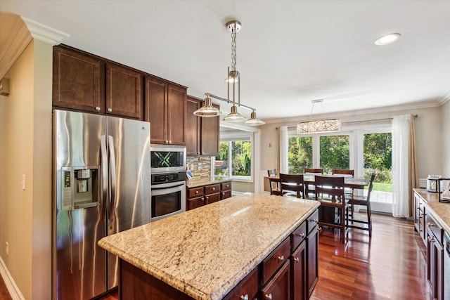 kitchen featuring dark wood-type flooring, hanging light fixtures, stainless steel appliances, crown molding, and a kitchen island