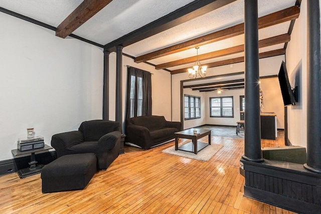 living room with beam ceiling, ornate columns, ceiling fan with notable chandelier, and light wood-type flooring