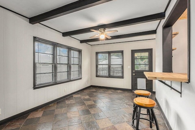 interior space with beam ceiling, ceiling fan, and wood walls