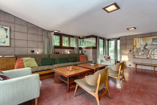 living room with concrete floors, vaulted ceiling, and tile walls