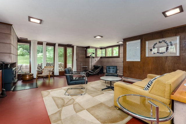 living room featuring concrete flooring, a baseboard heating unit, a healthy amount of sunlight, and wood walls