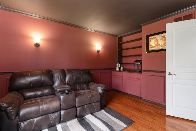 home theater room featuring built in shelves, light wood-type flooring, and crown molding