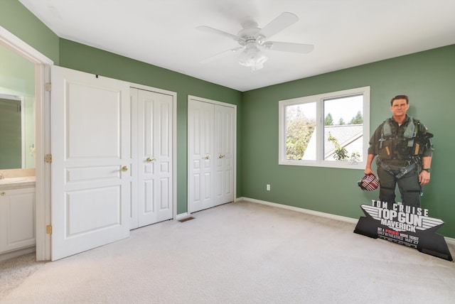 bedroom with light carpet, two closets, ensuite bath, and ceiling fan