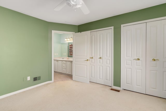 unfurnished bedroom with light carpet, ensuite bathroom, ceiling fan, and multiple closets