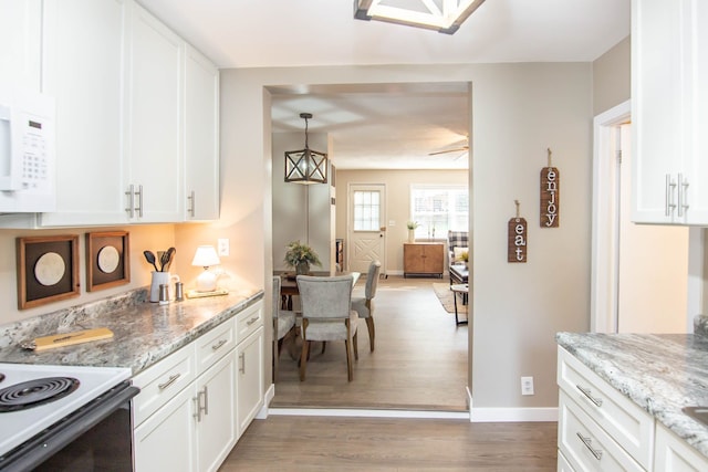 kitchen with white cabinets, light wood-type flooring, light stone counters, and hanging light fixtures