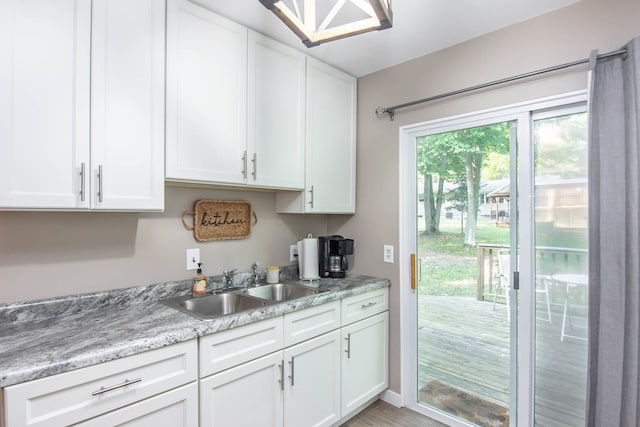 kitchen with light stone counters, light hardwood / wood-style floors, white cabinetry, and sink