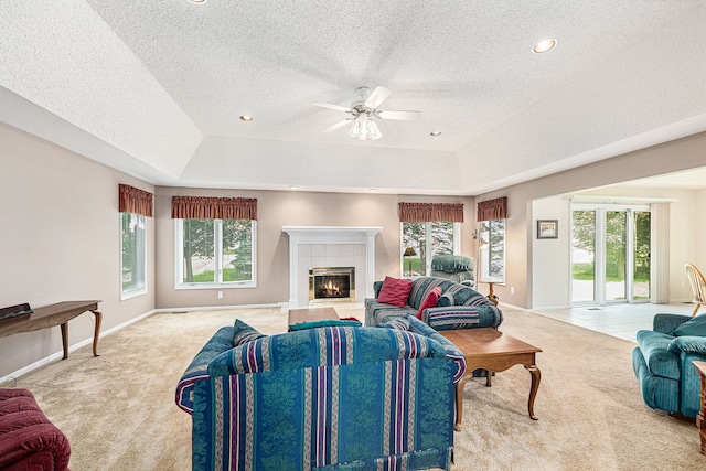 living room featuring light carpet, a tile fireplace, a raised ceiling, ceiling fan, and a textured ceiling