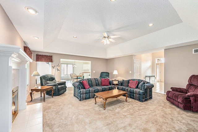 carpeted living room with a tile fireplace, a textured ceiling, a tray ceiling, and ceiling fan