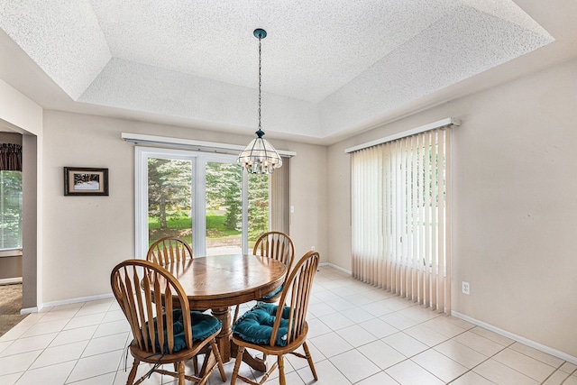 tiled dining space featuring a raised ceiling, a textured ceiling, and an inviting chandelier