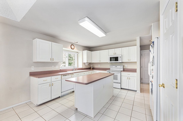 kitchen with a center island, white appliances, sink, light tile patterned flooring, and white cabinetry