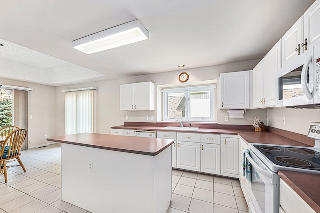 kitchen featuring white appliances, sink, light tile patterned floors, a kitchen island, and white cabinetry