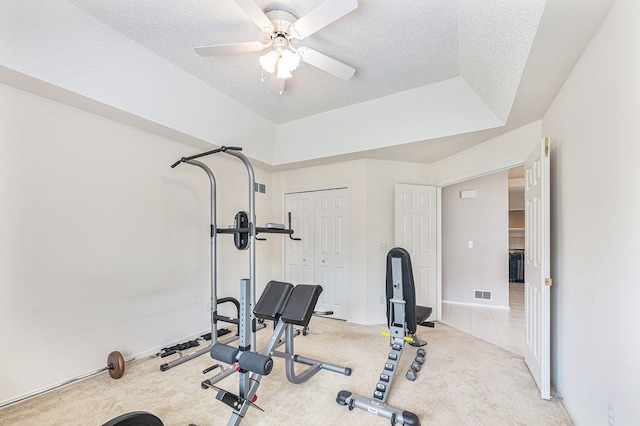 workout room with a tray ceiling, light carpet, ceiling fan, and a textured ceiling