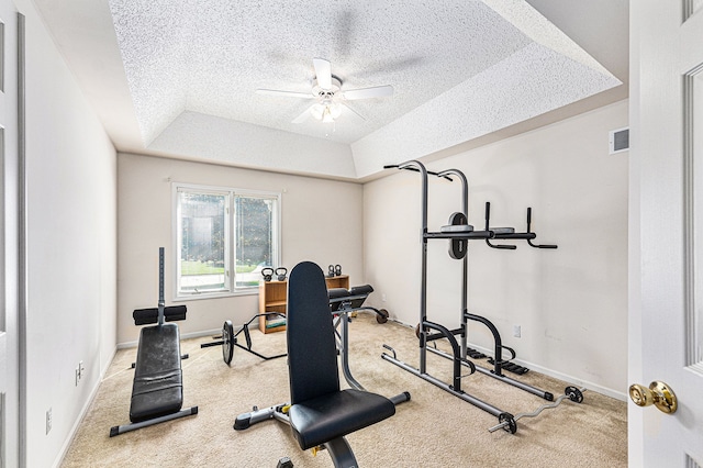 exercise room with a tray ceiling, ceiling fan, light colored carpet, and a textured ceiling