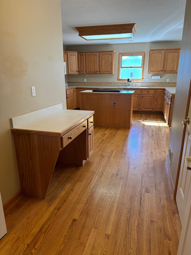 kitchen with cooktop, a textured ceiling, a center island, and light hardwood / wood-style flooring