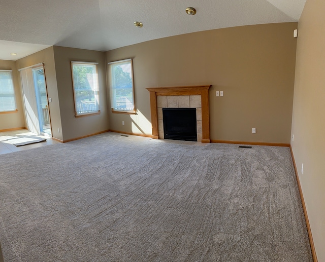 unfurnished living room with light colored carpet, a textured ceiling, and a tile fireplace